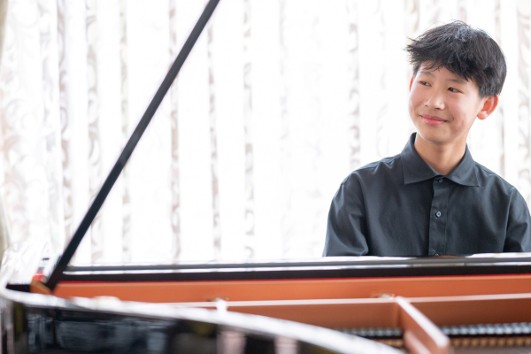 A teenage pianist seated at a grand piano, smiling and looking to the side
