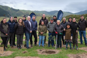 A group of Greater Wellington representatives, mana whenua, community members and volunteers gather beside a newly planted native tree at Queen Elizabeth Park.