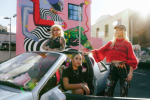 Dreamgirls Art Collective members pose beside a car in front of a colourful Matariki-inspired mural in central Wellington.