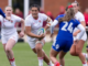 An England women’s age-group rugby player carries the ball towards a defender in blue during a match.