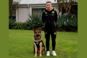 Wellington Phoenix women’s head coach Bev Priestman stands beside newly qualified Police patrol dog Phoenix FC on a lawn.