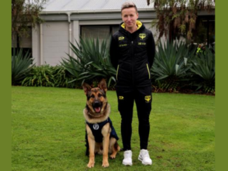 Wellington Phoenix women’s head coach Bev Priestman stands beside newly qualified Police patrol dog Phoenix FC on a lawn.