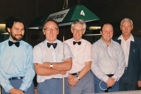 Russell Robinson, second from right, stands with four fellow billiards and snooker players beside a competition table.