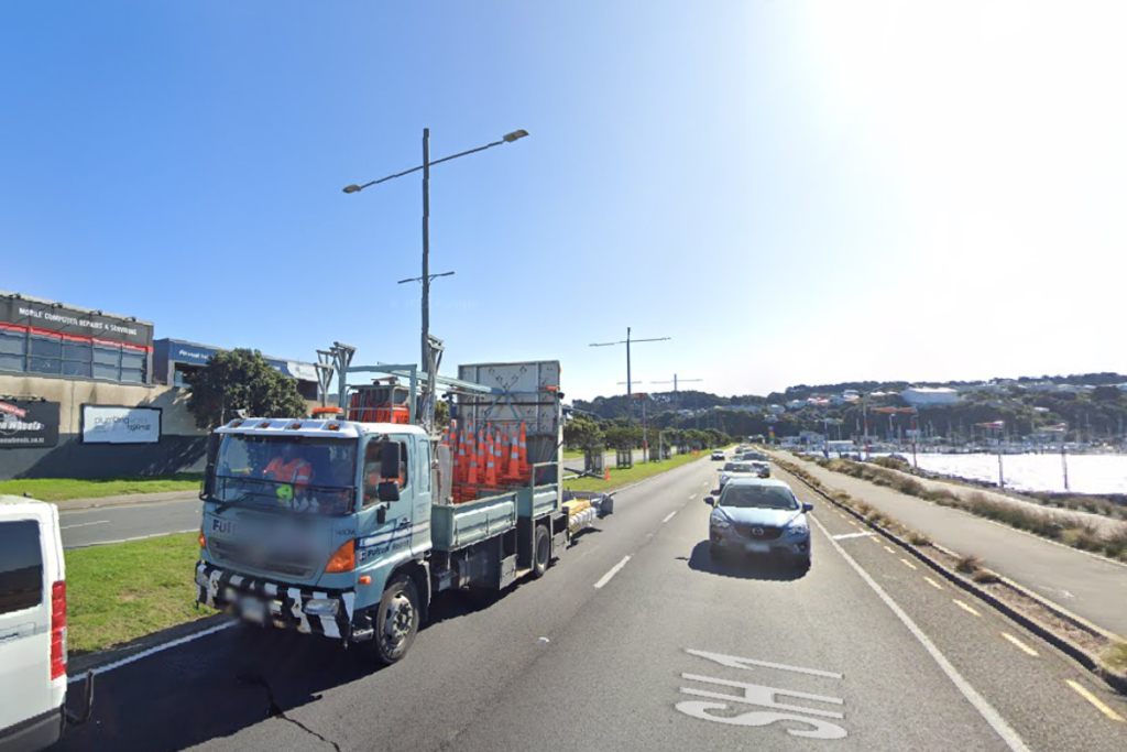 Traffic travelling along Cobham Drive in Wellington, with a roadworks truck carrying traffic cones in the foreground.