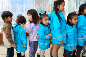 Children wearing rain jackets line up together during a school lunch programme.