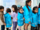 Children wearing rain jackets line up together during a school lunch programme.