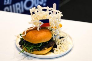 Lazy Juan’s Marites burger, winner of Burger Wellington 2026, topped with a Philippine flag and served with crispy rice noodles.