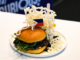 Lazy Juan’s Marites burger, winner of Burger Wellington 2026, topped with a Philippine flag and served with crispy rice noodles.