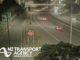 Night-time traffic travelling on Wellington’s urban motorway beneath an overbridge, with illuminated road signs and a 100km/h speed display.