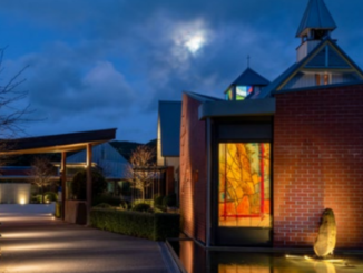 Our Lady’s Home of Compassion in Island Bay at dusk, with an illuminated stained-glass artwork by John Drawbridge visible in the chapel.