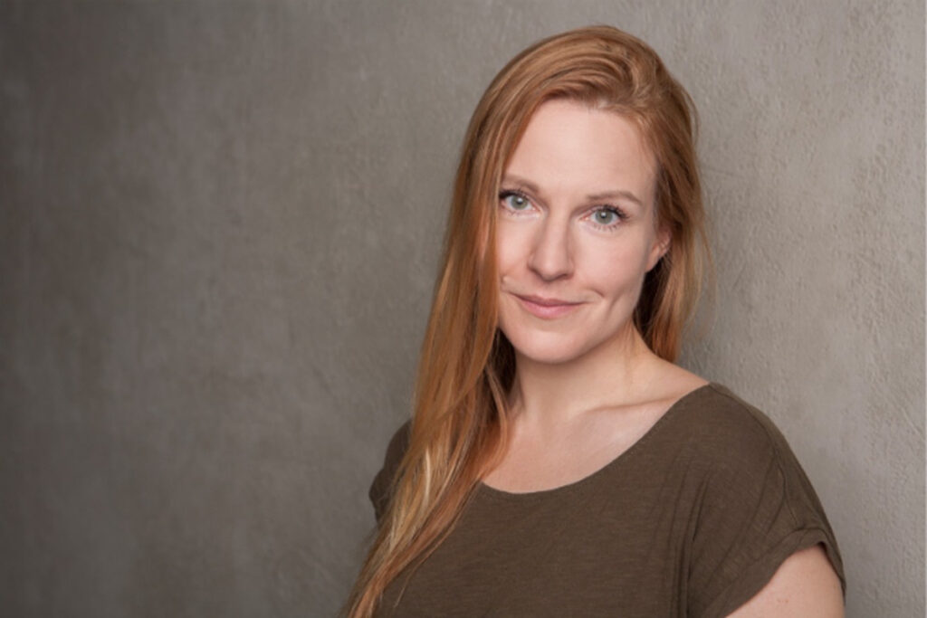 Writer Alice Miller standing against a grey wall.