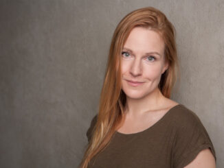 Writer Alice Miller standing against a grey wall.