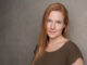 Writer Alice Miller standing against a grey wall.