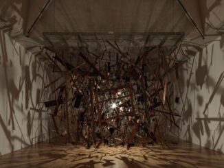 The remains of a garden shed suspended around a light in a gallery room, with the fragments casting long shadows across the walls.