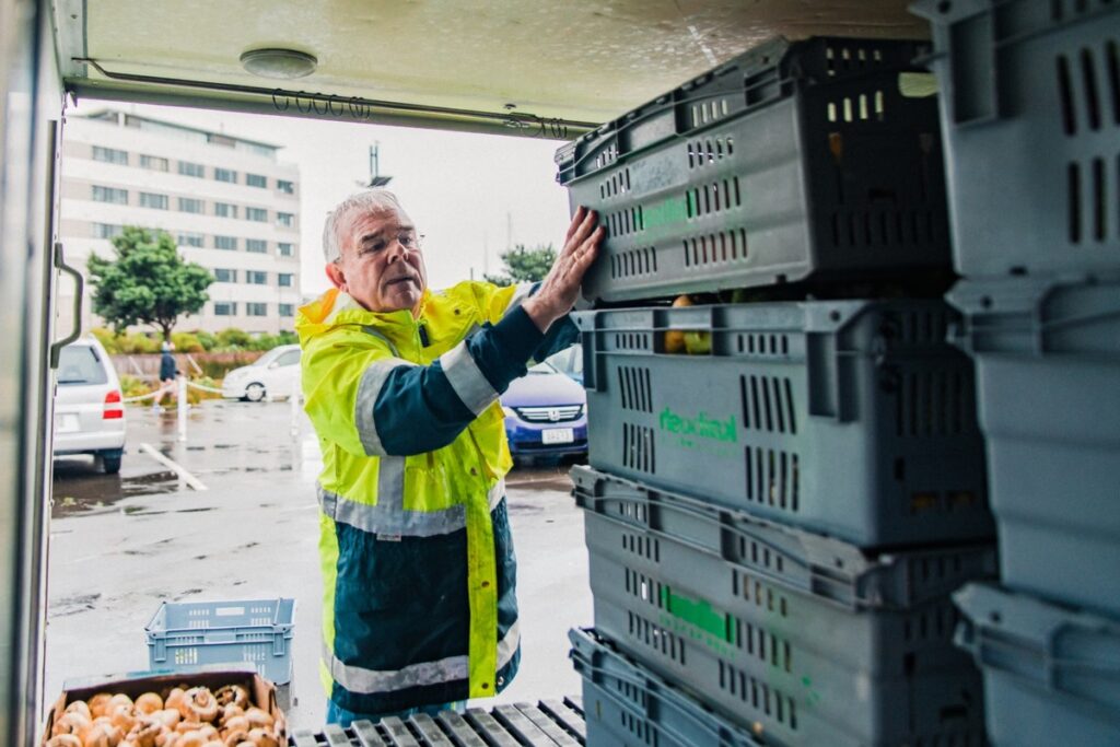 A person in a high-visibility raincoat handling stacked produce crates inside a van.